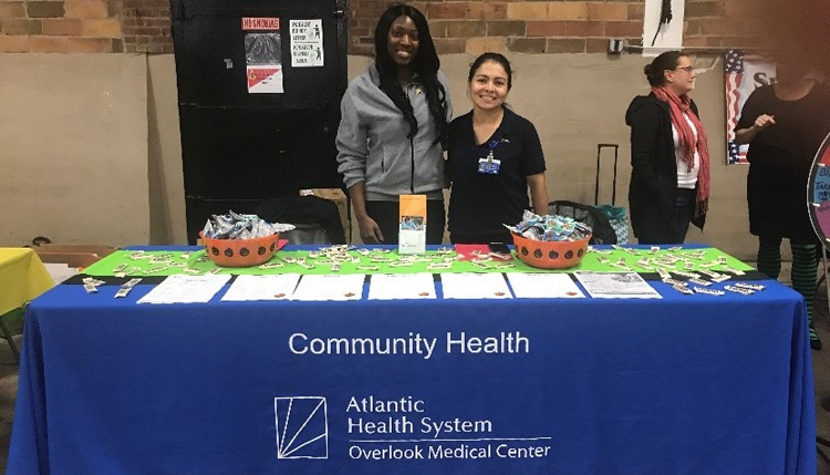 Tiffany Taylor (Health Educator) and Paula Garcia-Milla (Health Educator) standing behind an information table for dental hygiene and hand wash education.