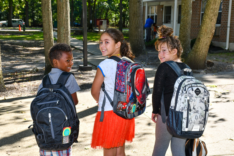 Small group of school children facing backwards with their backpacks.