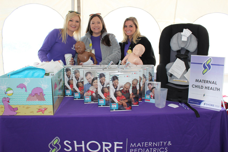 Shore Medical Center maternity department staff posing behind table with brochures and infant items while holding infant CPR dolls.