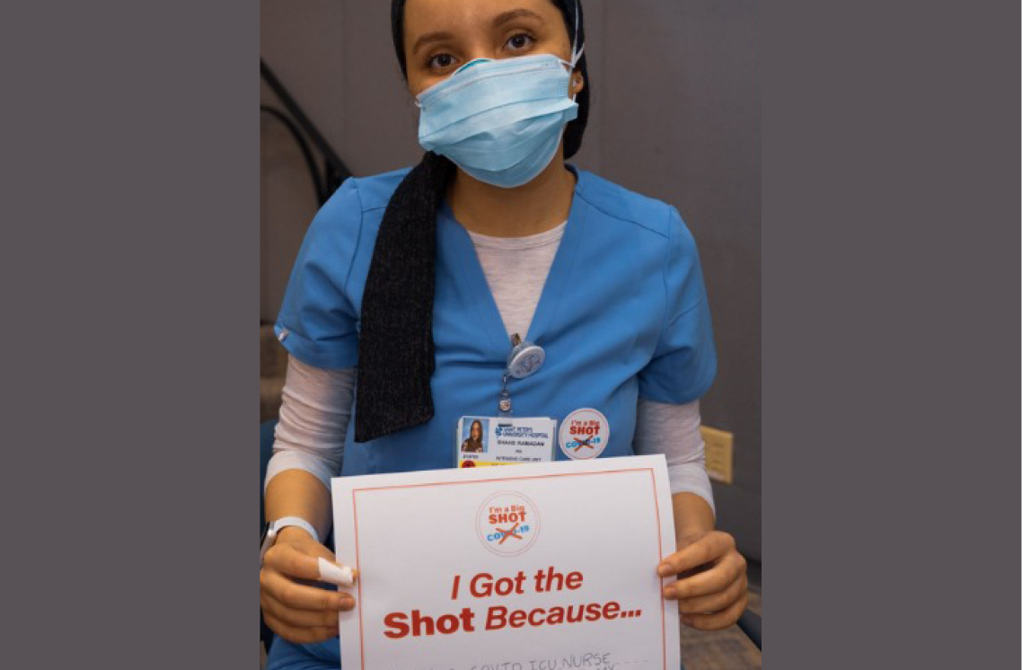 Female healthcare worker wearing a I'm a Big Shot sticker and holding I Got the Shot sign.