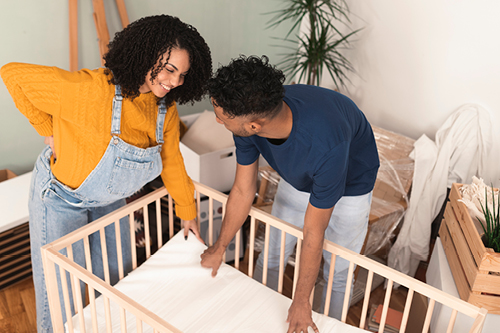 Pregnant woman and a man setting up a baby's crib.